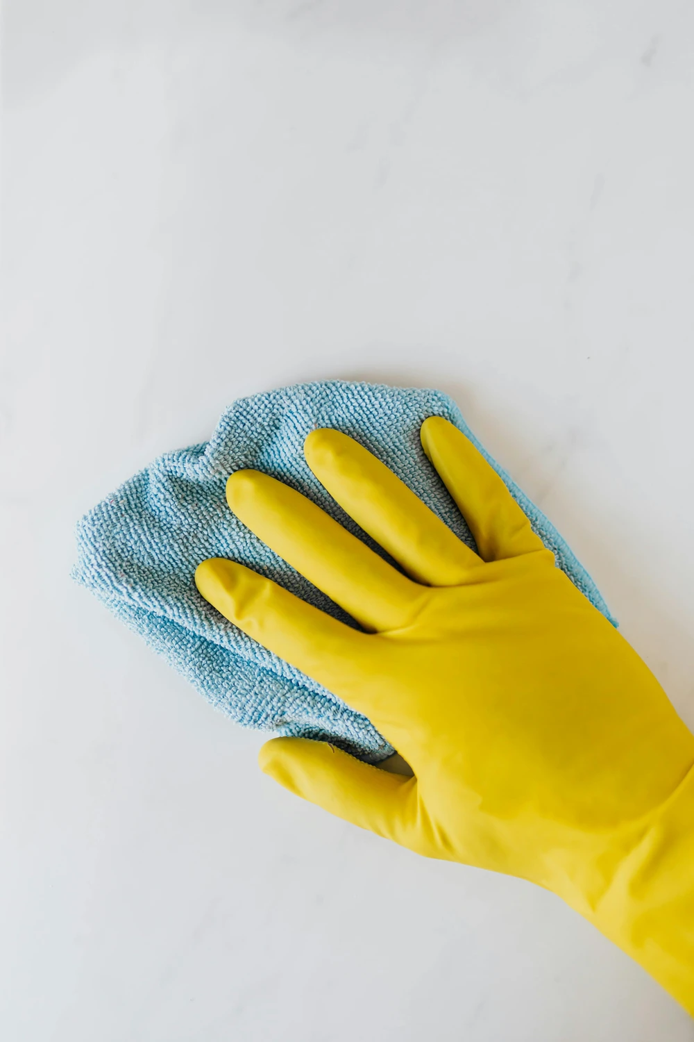 Simply Clean Niederrhein - Professionelle Reinigung - Eine Person, die einen leuchtend gelben Gummihandschuh trägt, wischt eine weiße Oberfläche mit einem blauen Mikrofasertuch ab.
